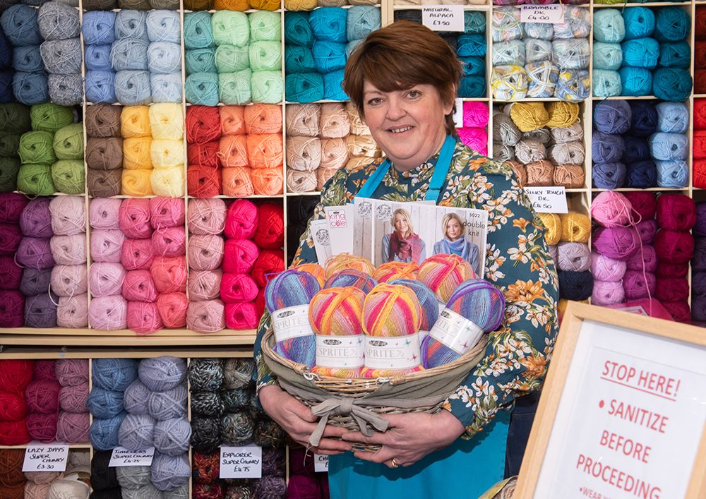 Sam Spence holding basket of wool in front shelves full of bright balls of wool